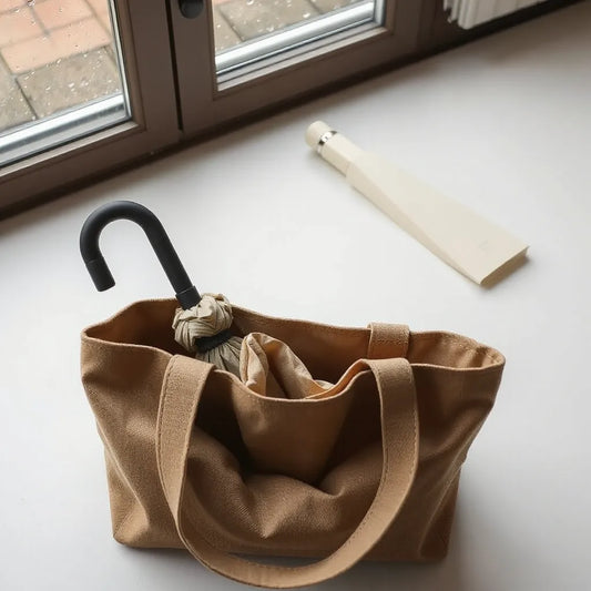 Kompakt paraply nerpackat i en öppen handväska, med mjuka regndroppar i bakgrunden